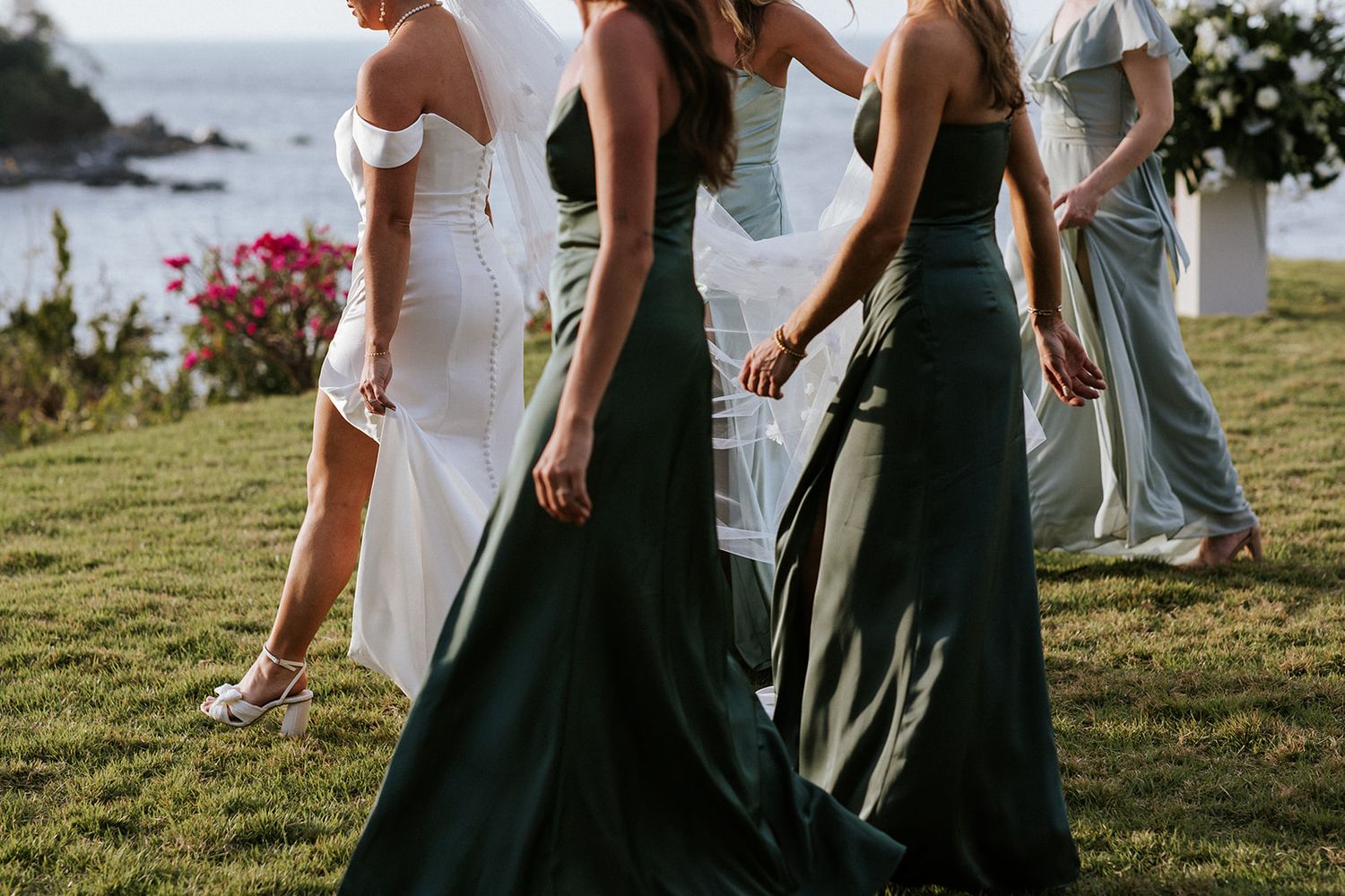 Bride and bridesmaids in satin gowns walking together by the ocean garden in Puerto Vallarta, by José Carrillo Photography.