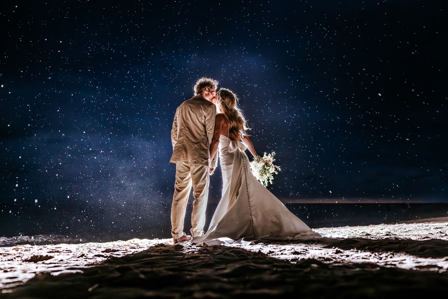 Newlyweds sharing a kiss under the rain on a Puerto Vallarta beach, illuminated beautifully by José Carrillo Photography.