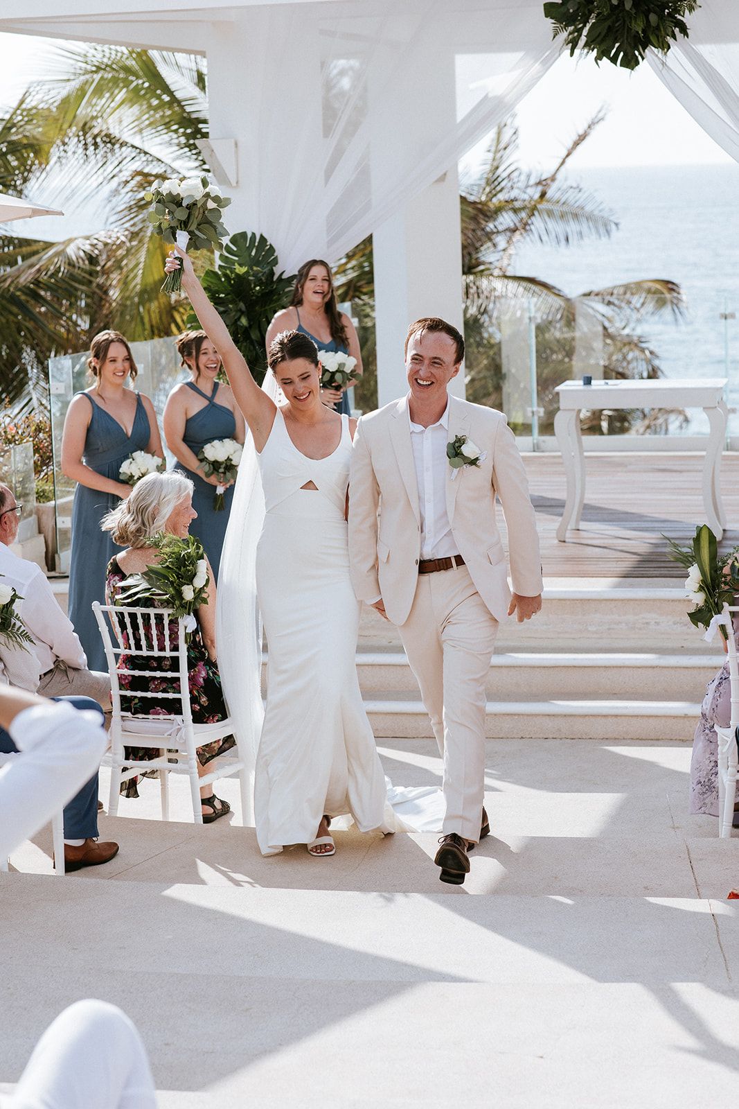 Bride raises bouquet in joy as newlyweds walk down the aisle after their beach ceremony in Puerto Vallarta, by José Carrillo.