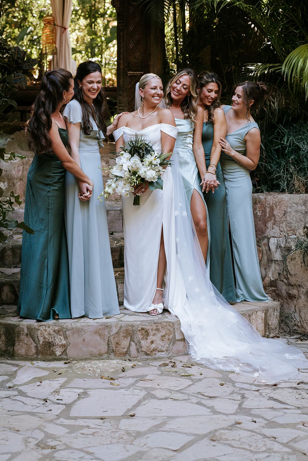 Bride and bridesmaids pose in pastel dresses surrounded by tropical garden beauty in Puerto Vallarta, by José Carrillo Photography.