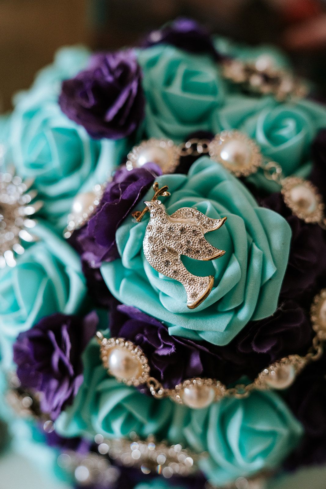 Luxury wedding detail with pearl jewelry and silver dove brooch on turquoise bouquet, captured by José Carrillo in Cabo San Lucas, Mexico.