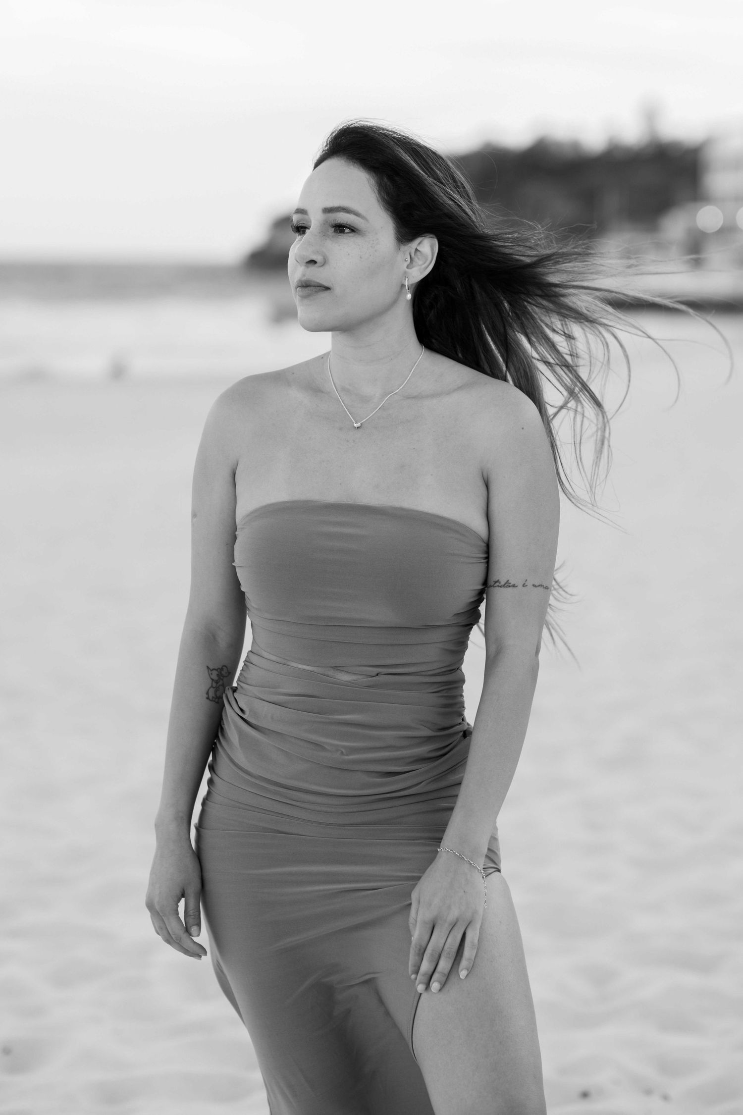 Black and white portrait of a woman in a flowing dress at Bondi Beach with wind blowing through her hair.