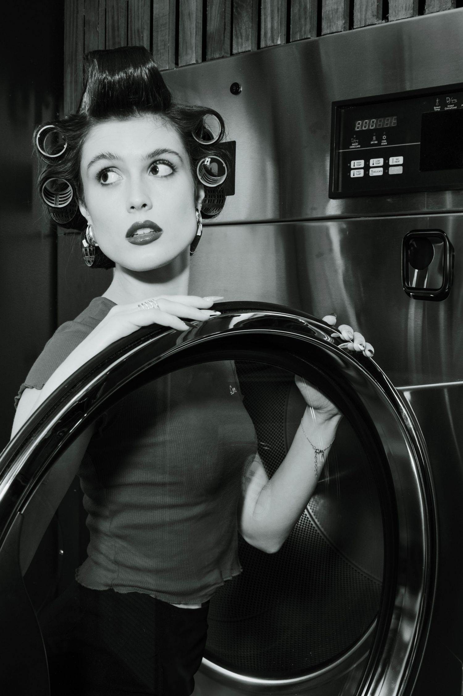 Editorial portrait of a woman with vintage hair rollers posing in a Ryde laundromat in black and white.