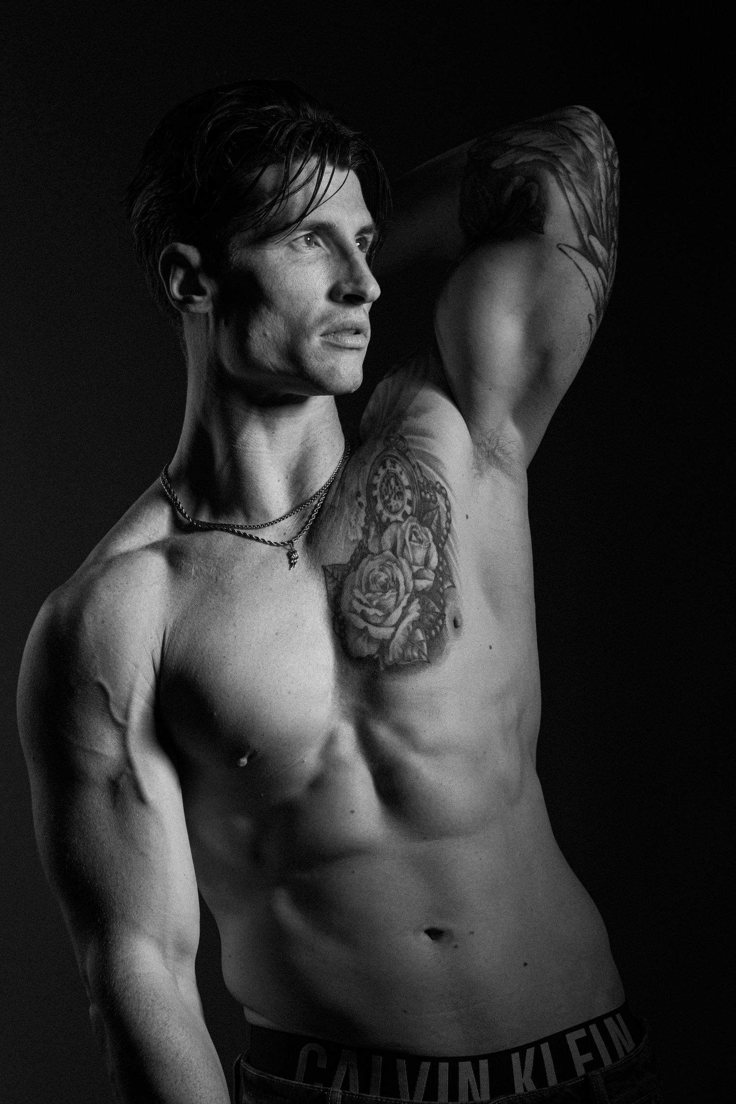 Black and white studio portrait of a male model using dramatic side lighting and shadow.