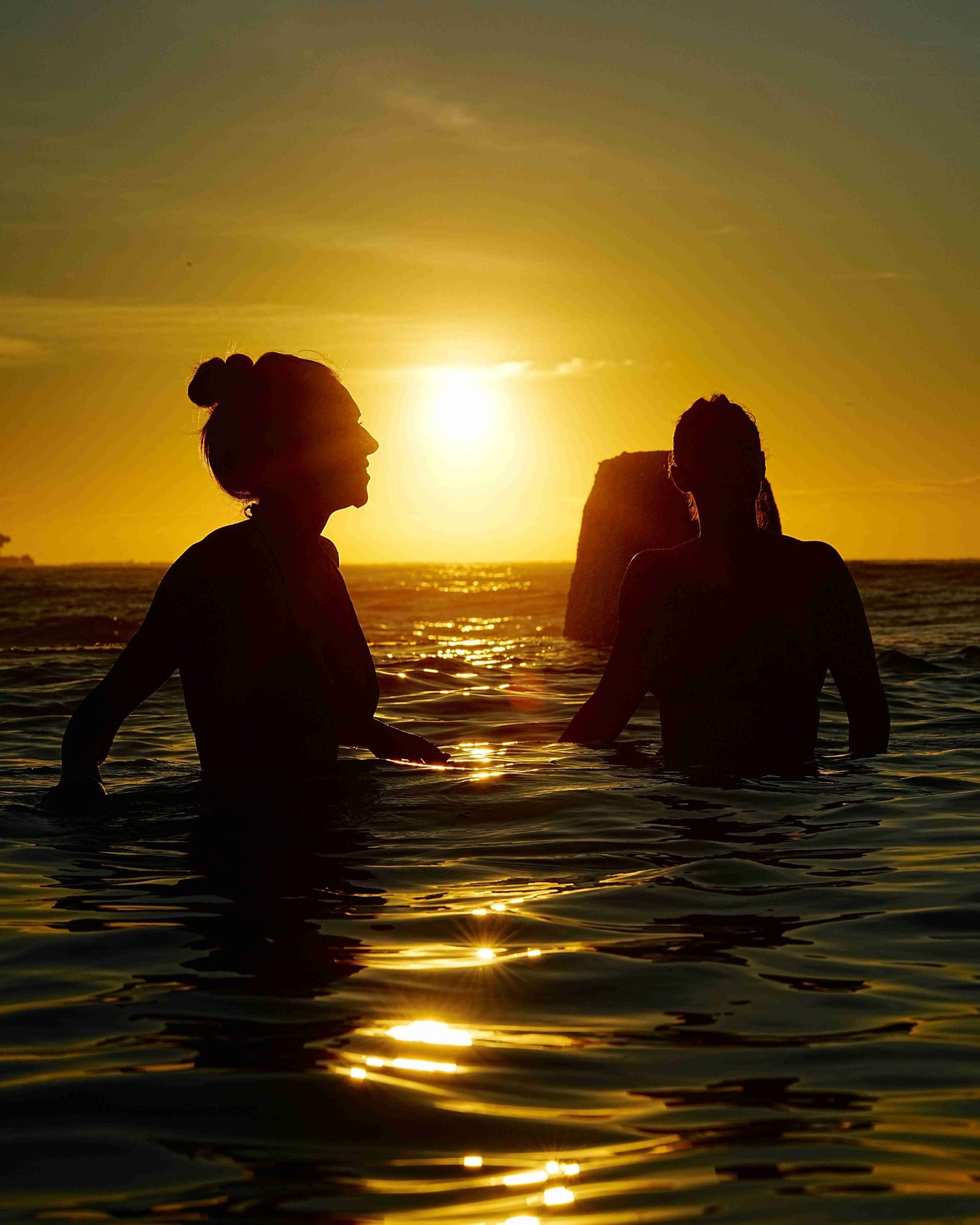 Sunrise portrait of two women silhouetted in Ross Jones Memorial Pool, Coogee, with golden light on the water.