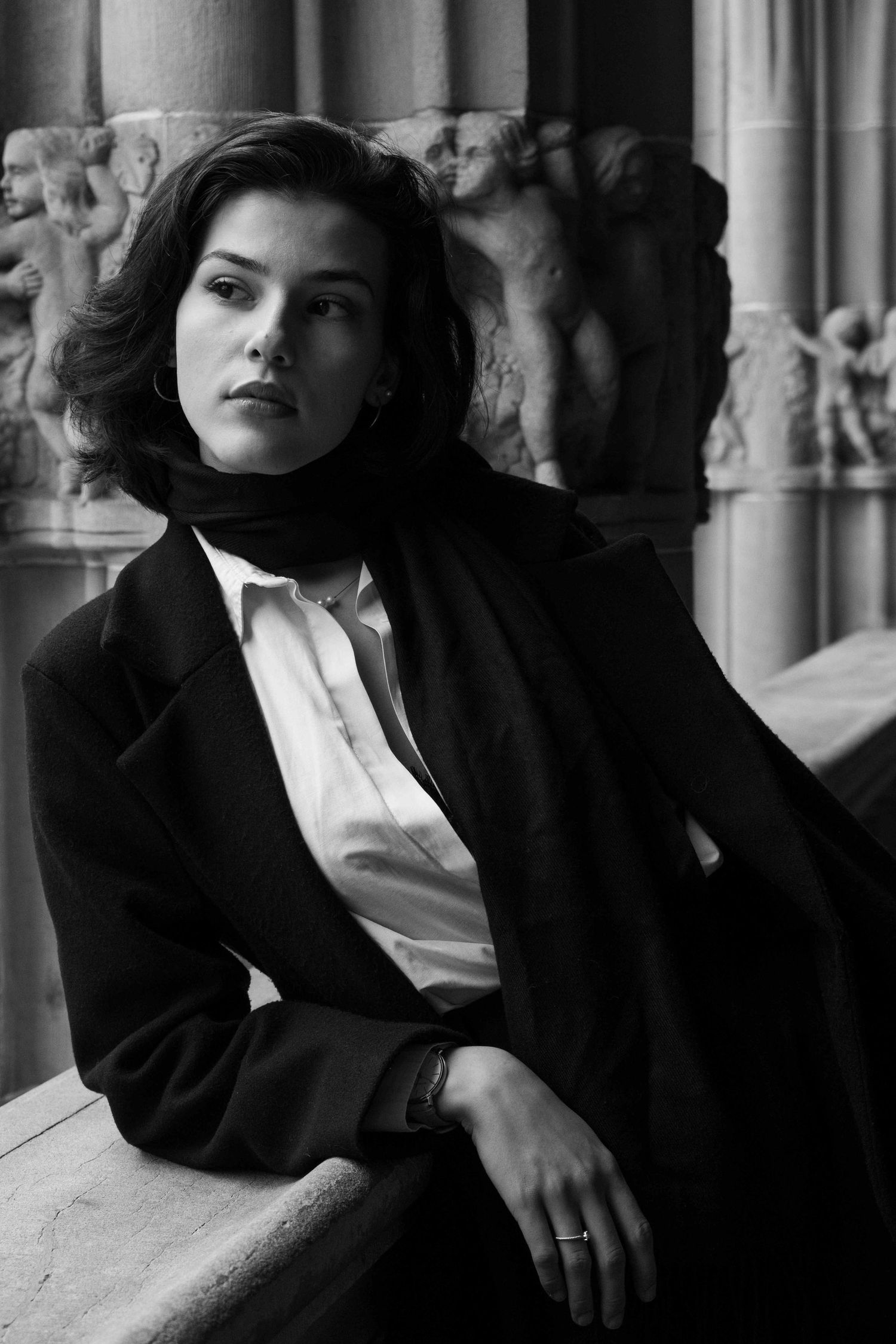 Black and white editorial portrait of a woman seated beside historic stone architecture in Zurich, Switzerland