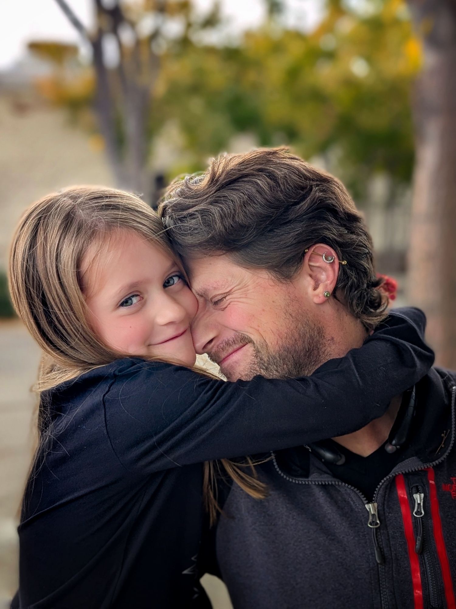 A tender moment captured outdoors with a loving embrace against an autumn background of trees. James Miller and Emma Miller Fall 2025.