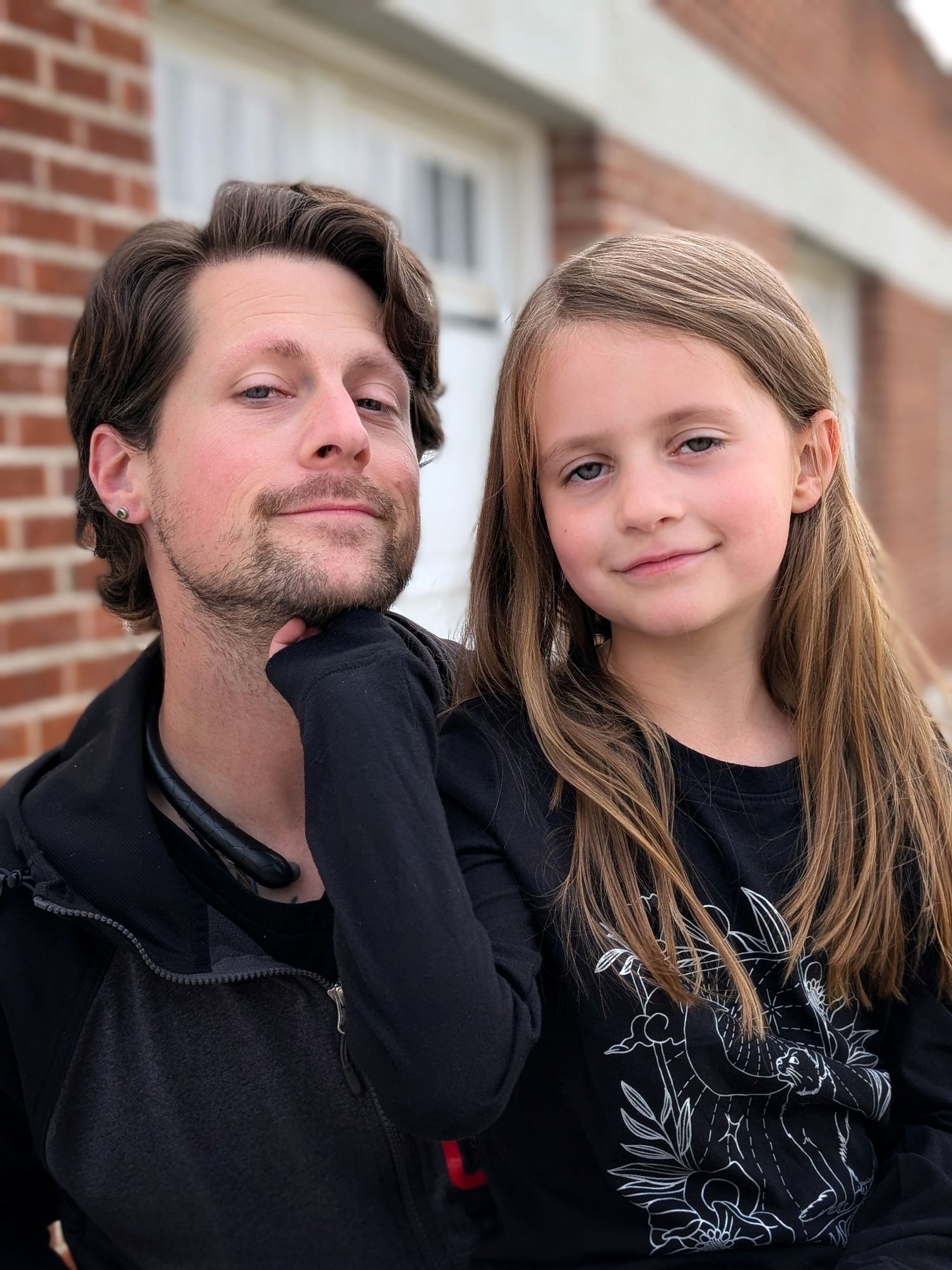 A series of five candid photos showing two people in black clothing posing playfully against a brick wall background.