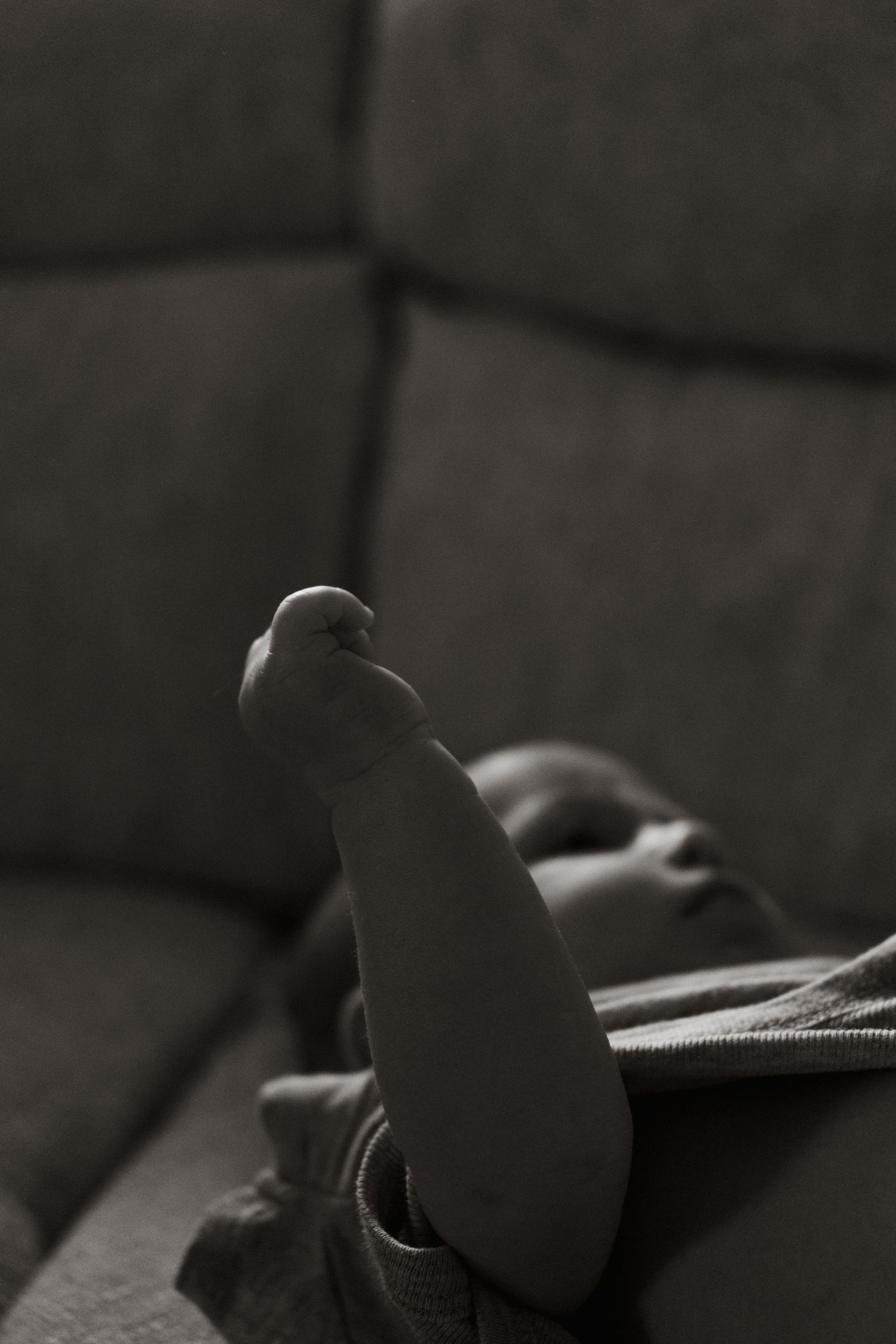 A close-up black and white photograph shows feet resting on a couch or sofa in a dimly lit room.