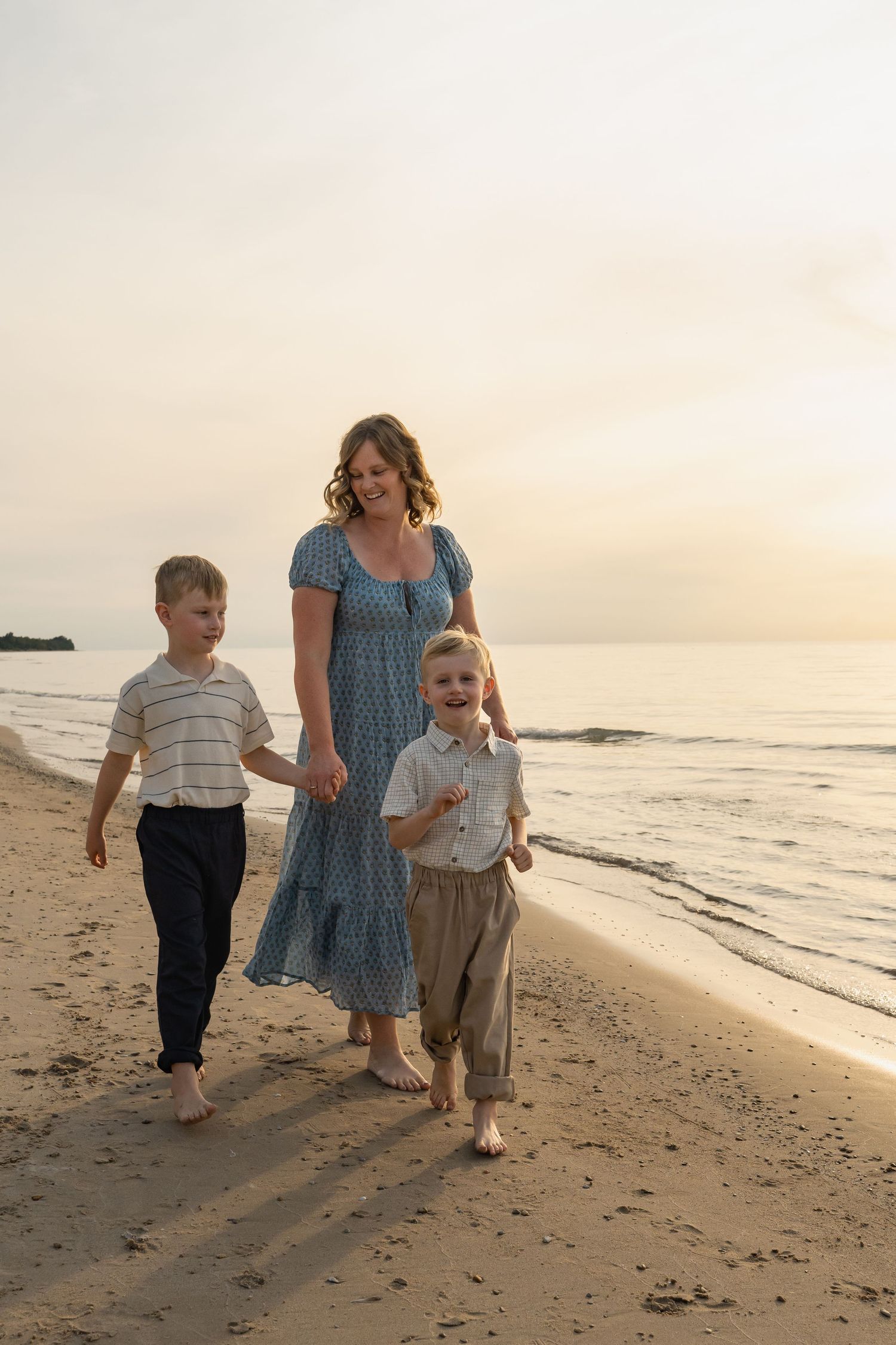 A family takes a sunset stroll along a peaceful beach shoreline, with waves gently lapping at the sand.