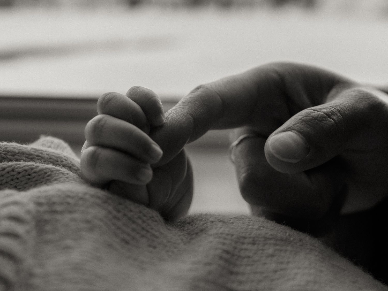 A tender black and white close-up photograph shows a tiny infant hand grasping an adult finger.