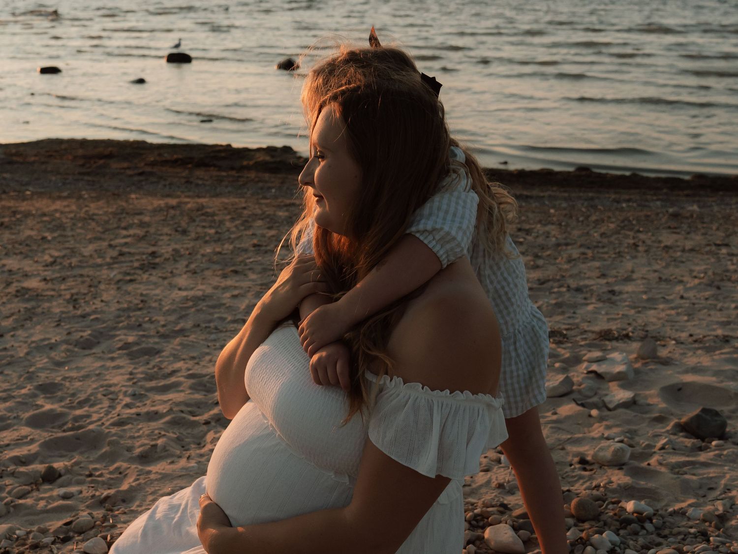 Family embracing on a sandy beach during golden hour with water in the background.
