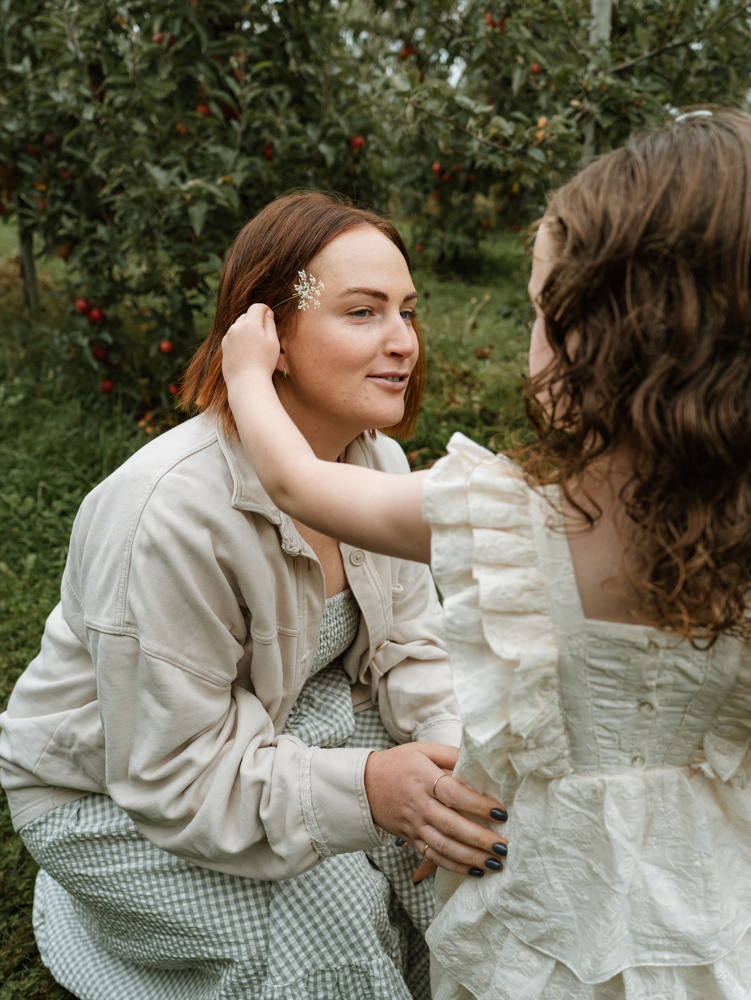 Two people in vintage-style white clothing share an intimate moment in a garden with apple trees in the background.