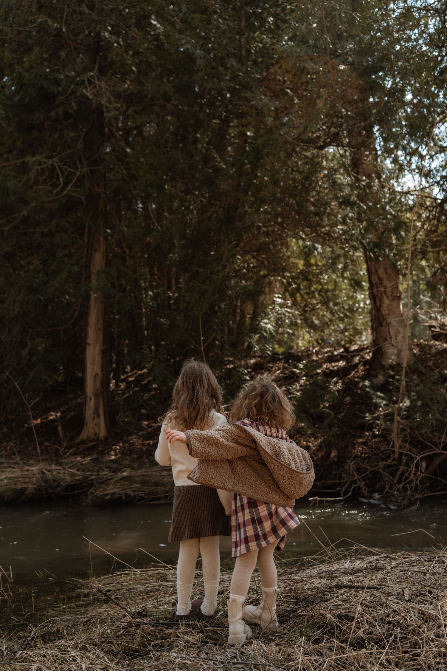 Two people exploring a wooded area wearing vintage-style dresses and boots.