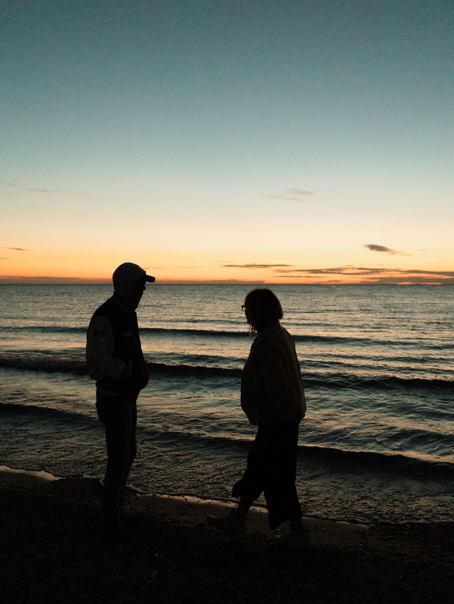Silhouettes of two figures walking along a beach at sunset with dramatic orange and teal sky reflections on the water.