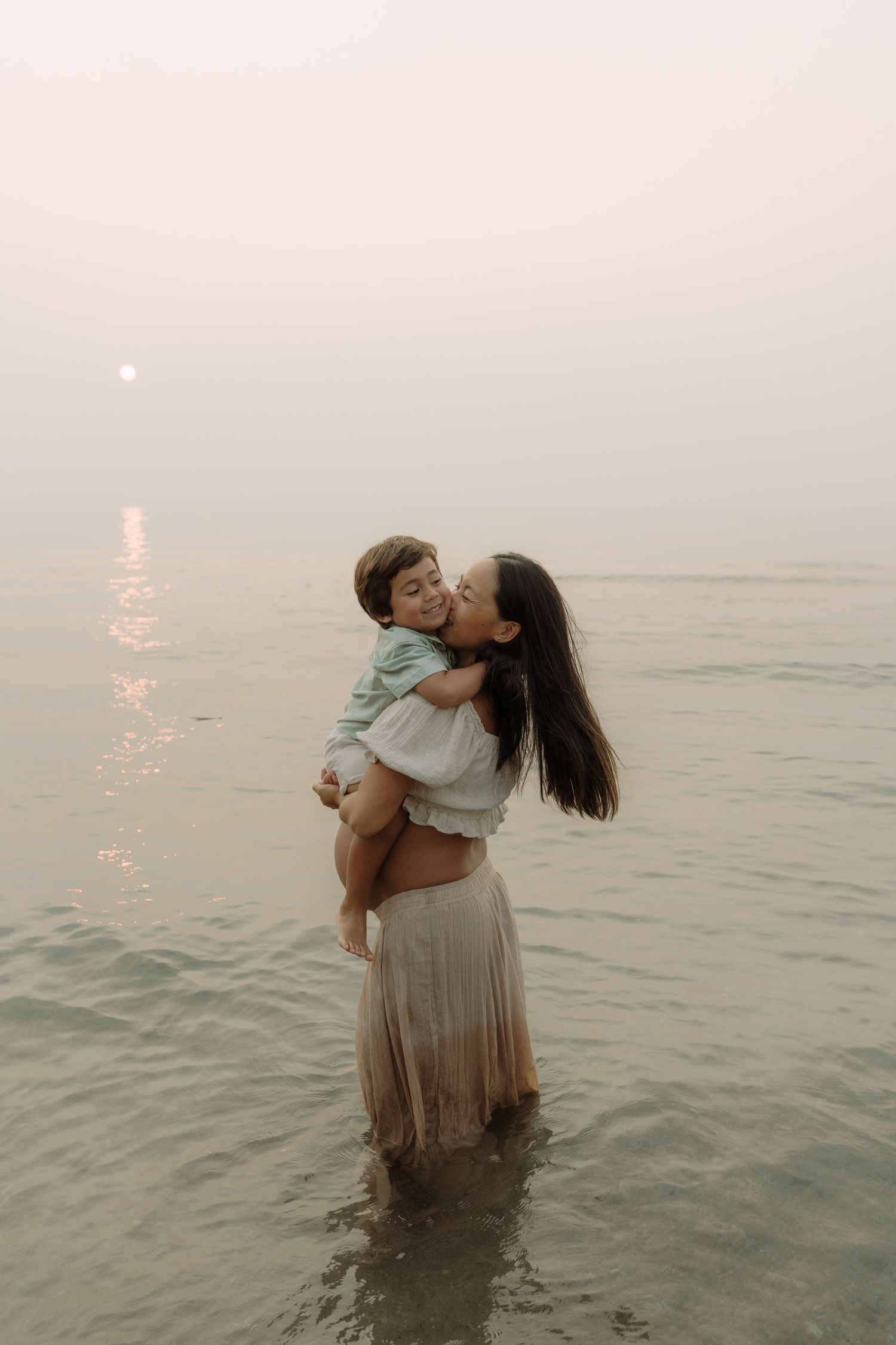 A couple embraces in shallow ocean water at dusk, creating a romantic silhouette against the misty horizon.