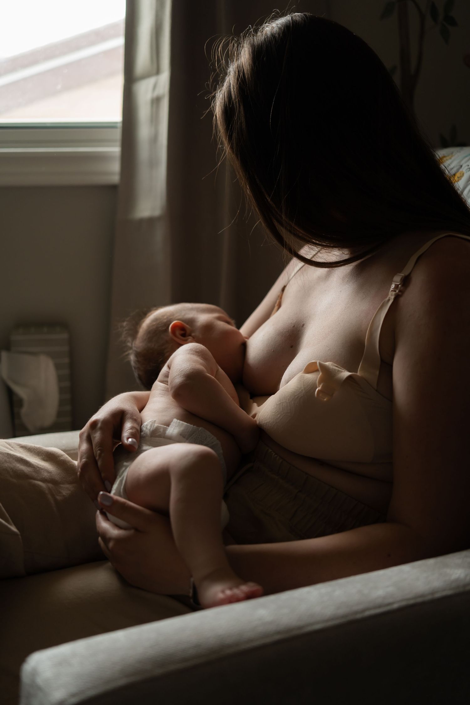 A tender nursing moment captured in soft window light creating an intimate atmosphere.