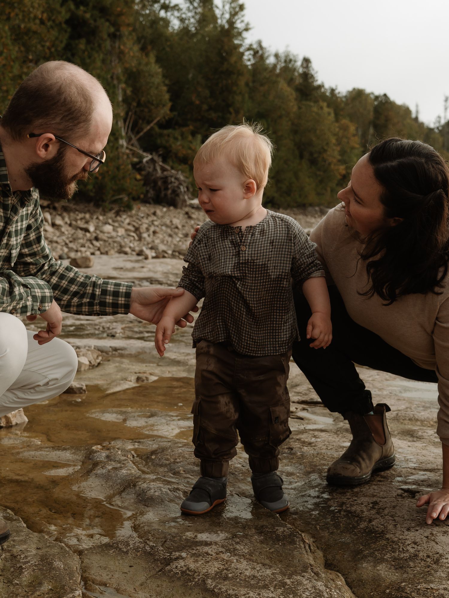 A parent and child explore a rocky riverbank together on an autumn day, creating special outdoor memories.