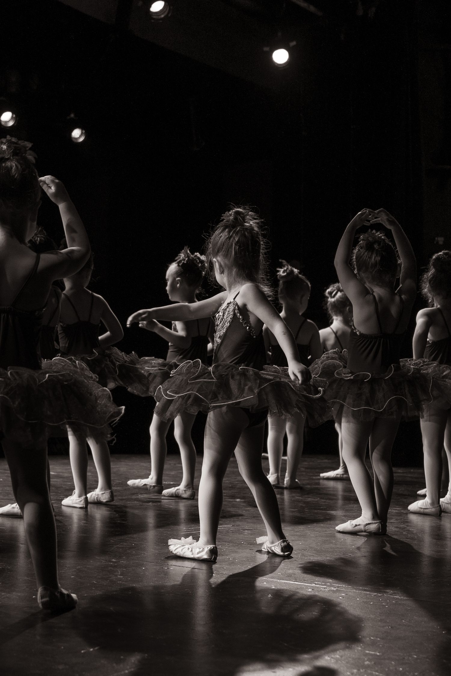 Ballet dancers practicing in a dark studio with dramatic lighting creating silhouettes on the stage floor.