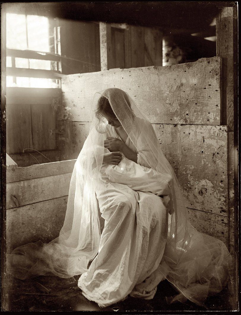 A vintage black and white photograph shows a figure in white robes and veil sitting in contemplation near a window.