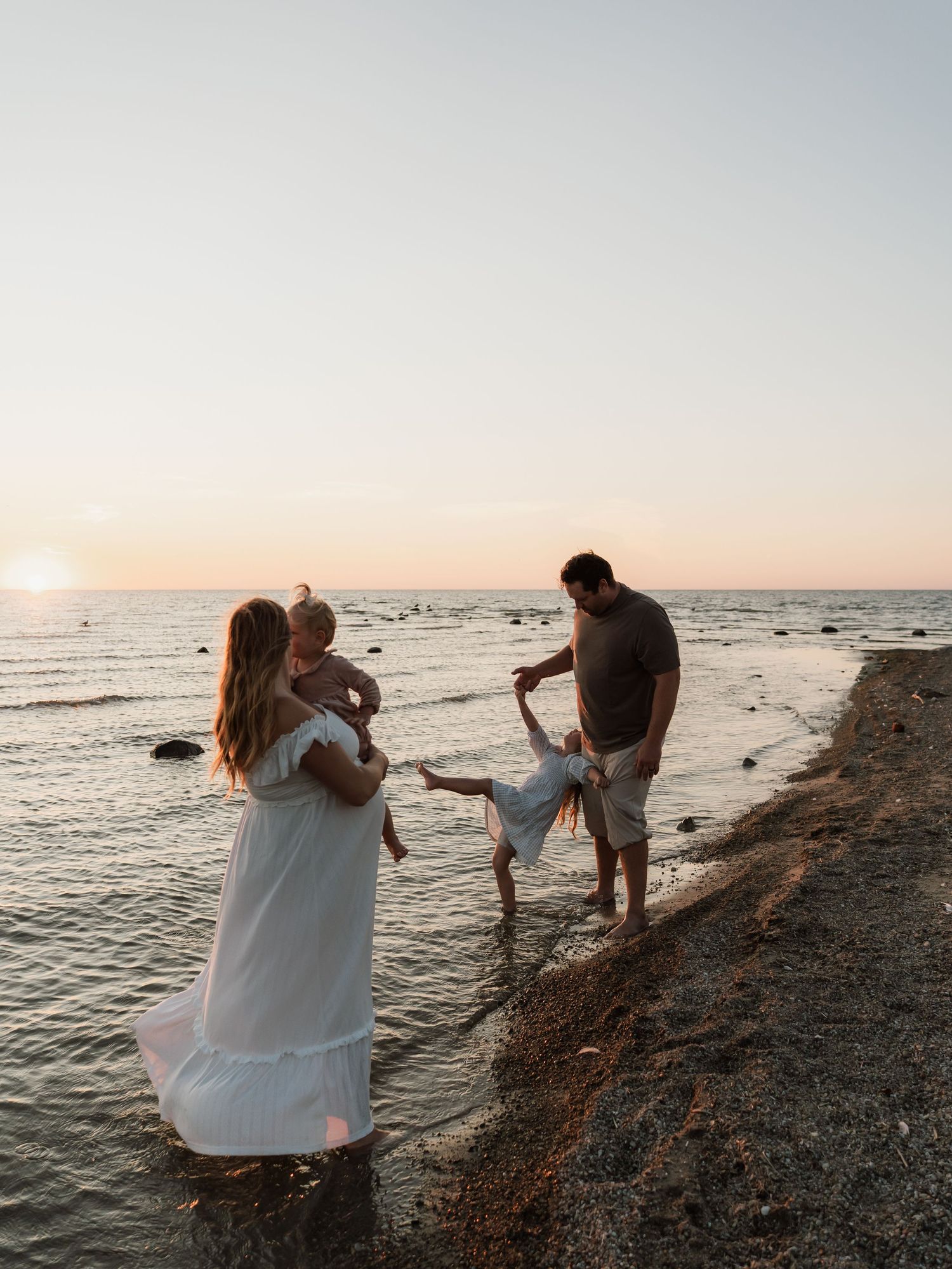 A couple shares a romantic moment on a rocky beach at sunset while taking photos together near the ocean.