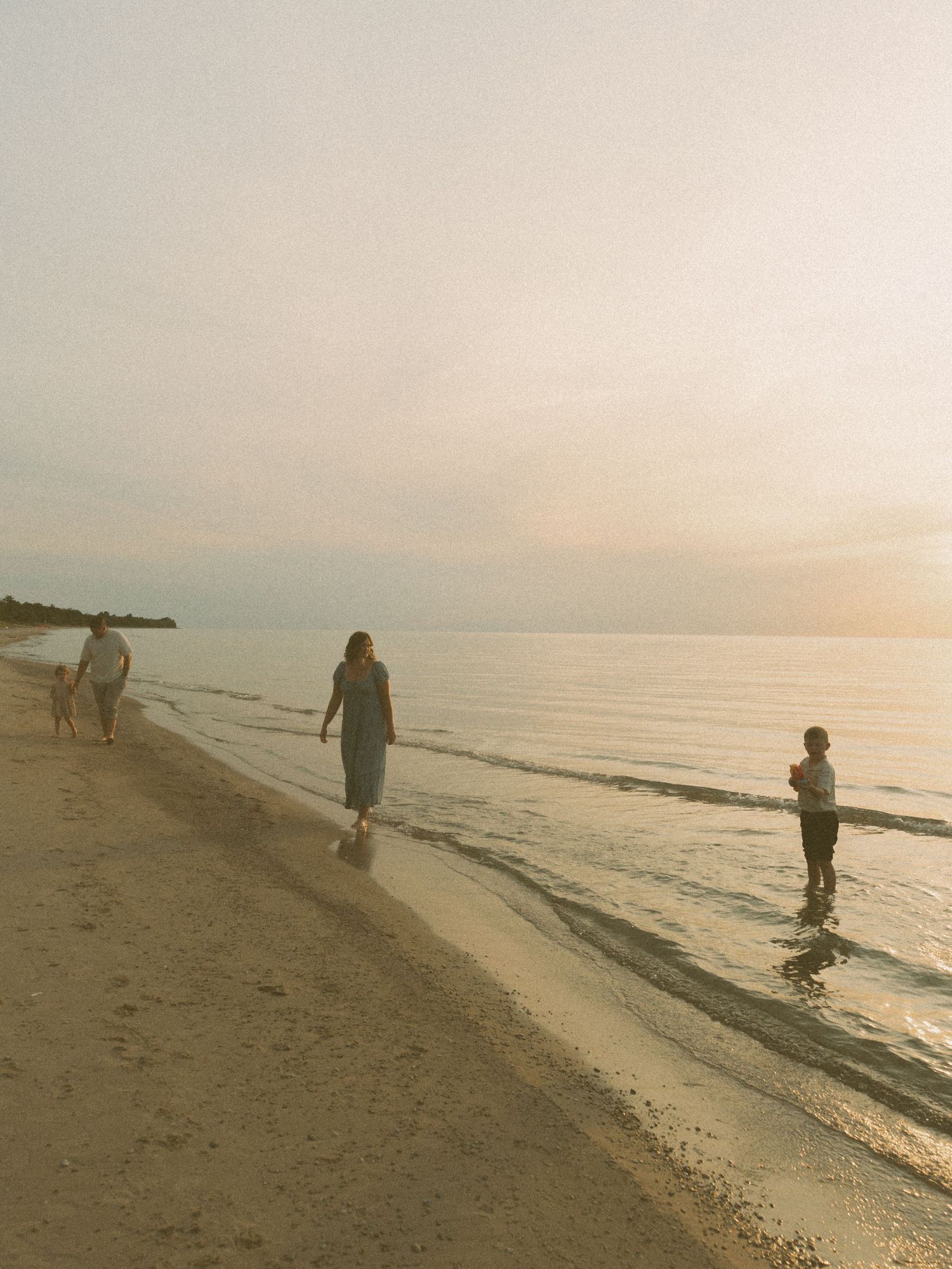 People walking along a peaceful beach at sunset with gentle waves lapping at the shore.