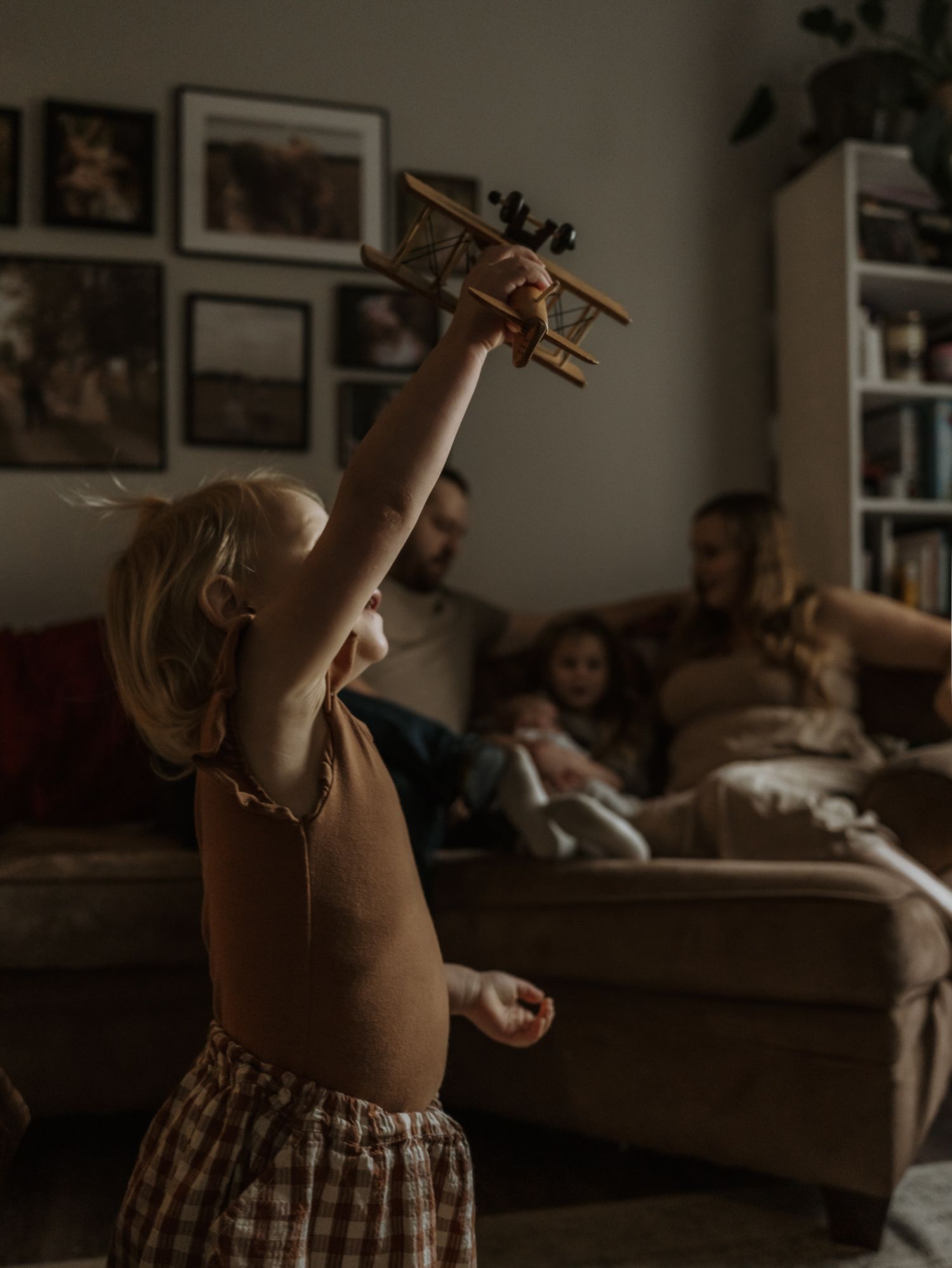 A wooden toy airplane being held up in a dimly lit room with a cozy atmosphere.
