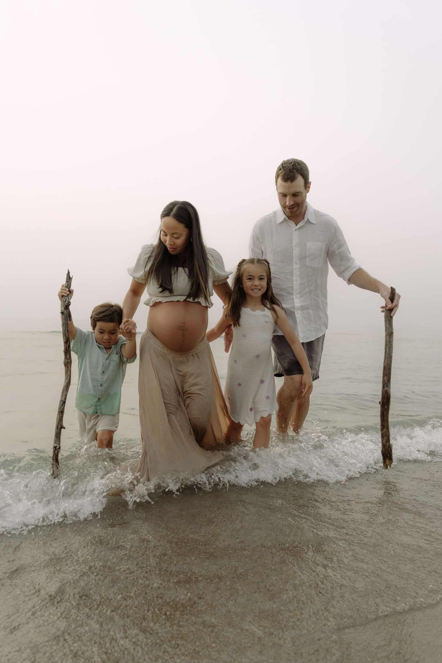 Family members wading through ocean waves while holding wooden posts during a beach activity.