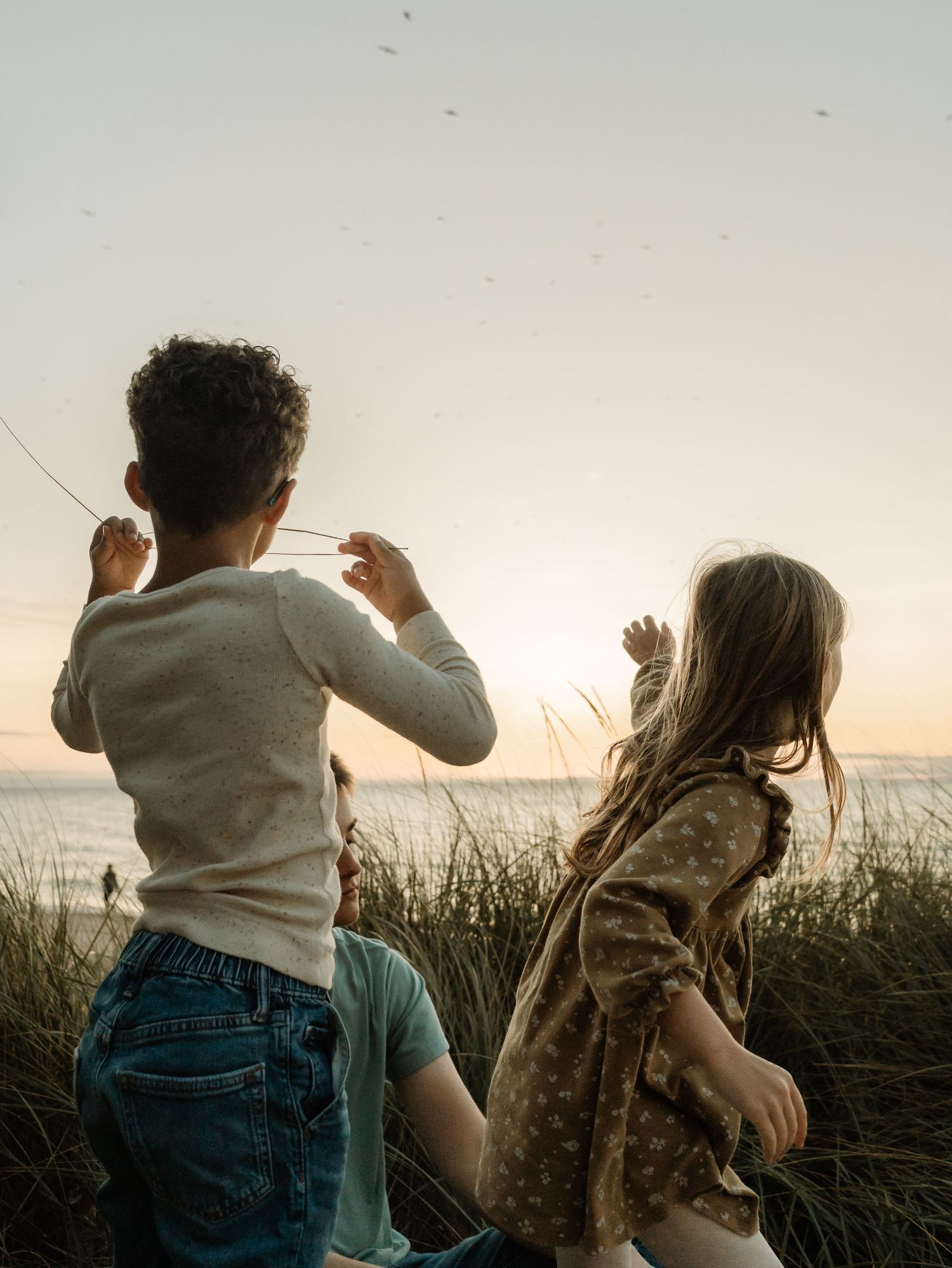 Silhouettes of people dancing together at sunset among tall grass by the ocean.