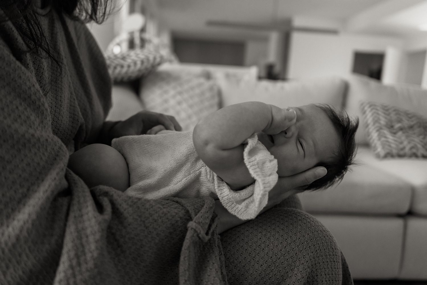 A tender black and white photo of a baby being cradled in someone's arms while lying on a textured blanket.
