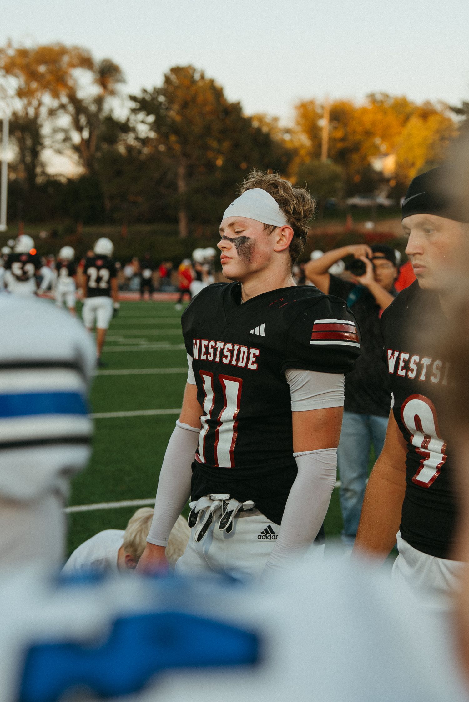 Westside football player #11 with eye black and head bandage stands on sideline during a high school game.