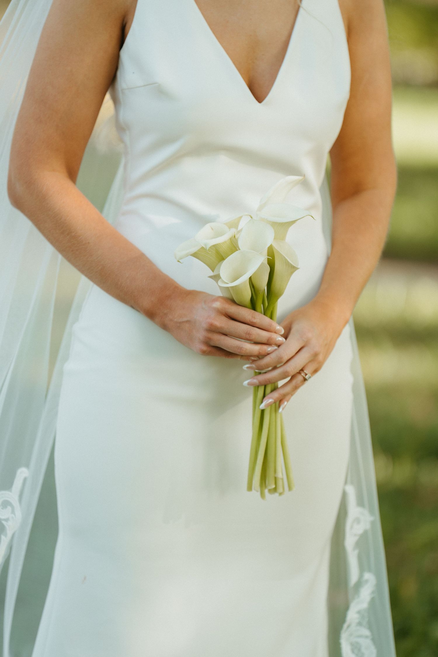 Close-up of white calla lily bouquet held against elegant wedding dress.