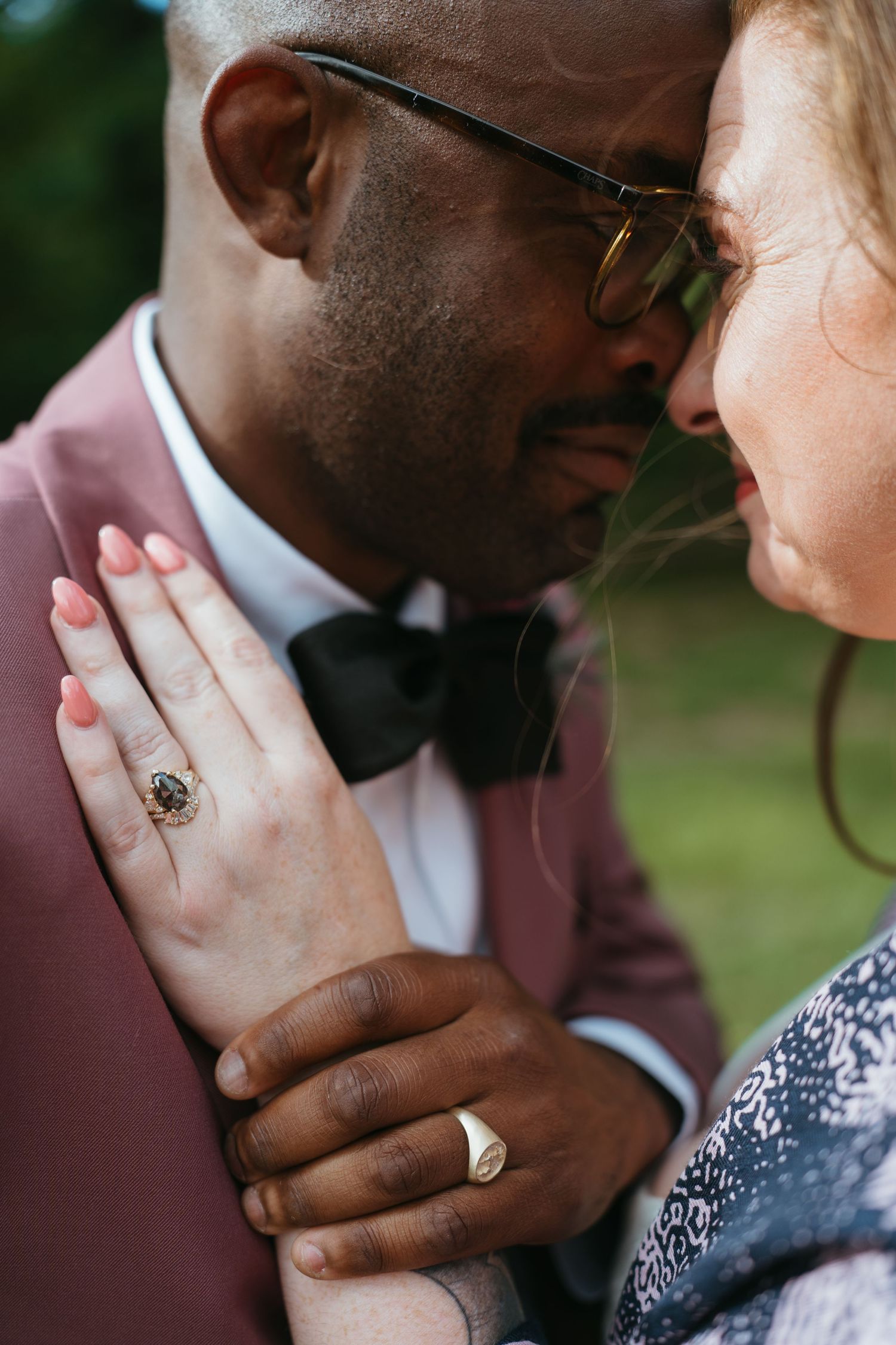 Interracial couple in formal wear share a tender moment, woman displaying elegant rings on her hand.