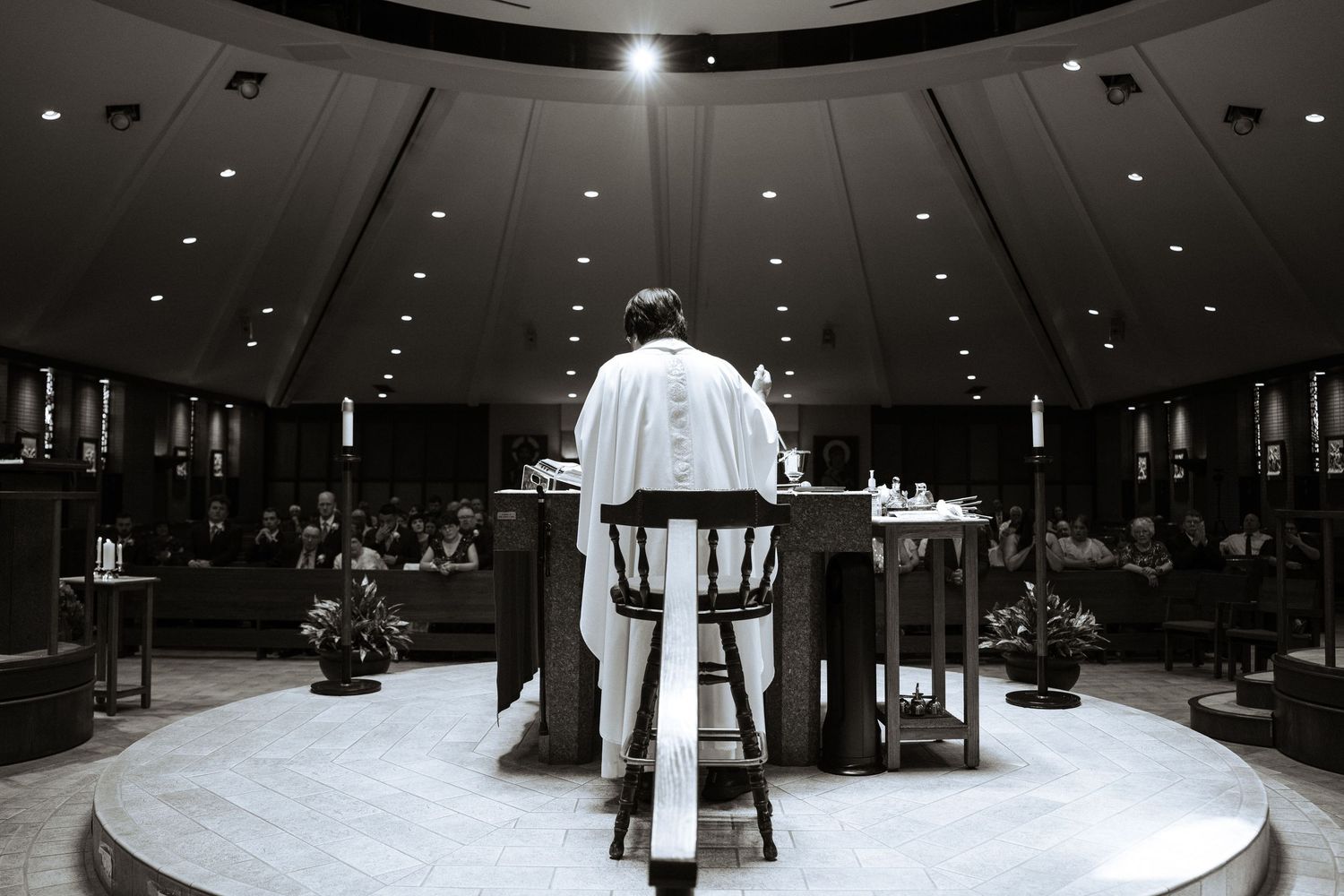 Black and white photo of a priest standing at an altar in a grand circular church filled with congregation.