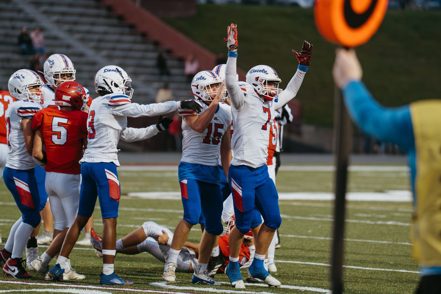Football players in blue and white uniforms celebrate on the field during a night game against a red-uniformed team.