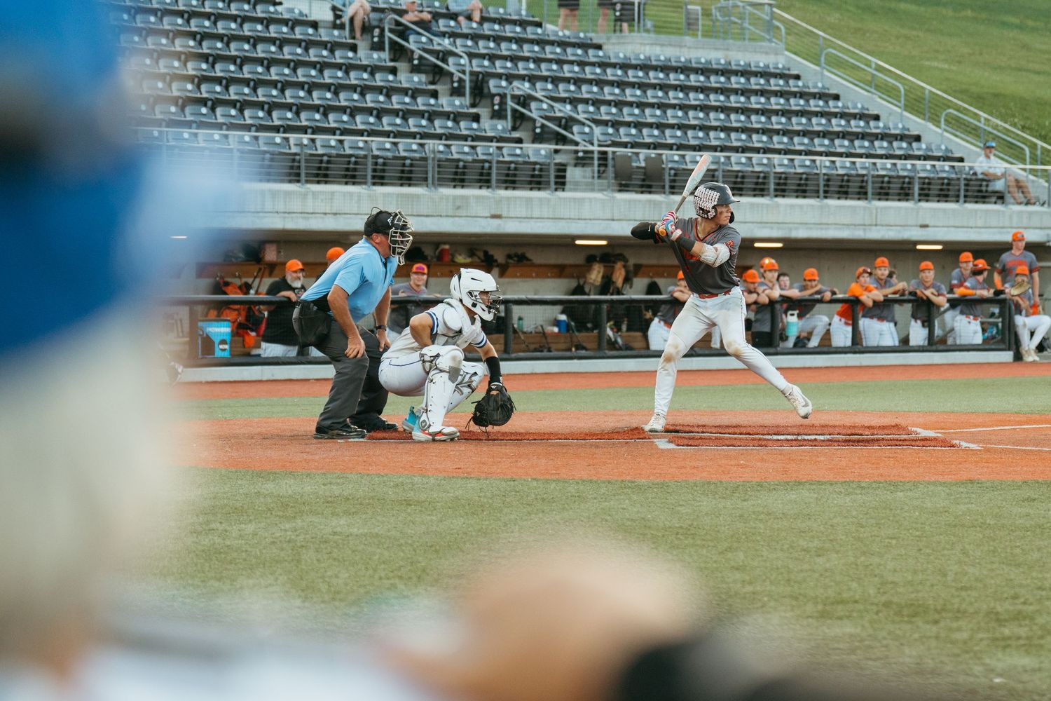 Baseball batter stands at home plate during a game at a stadium with spectators in the stands.