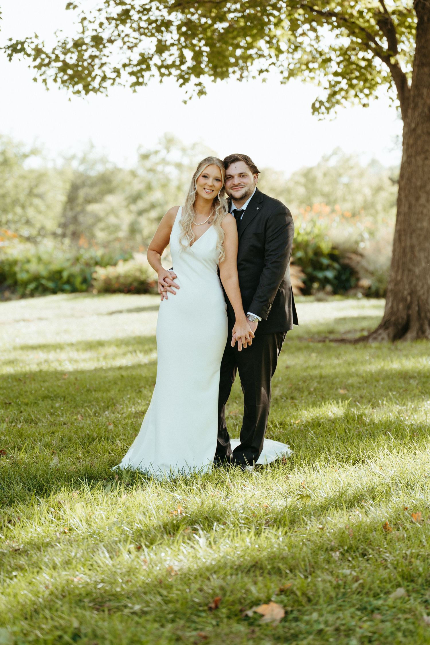 A couple in wedding attire sitting together on a grassy hillside.