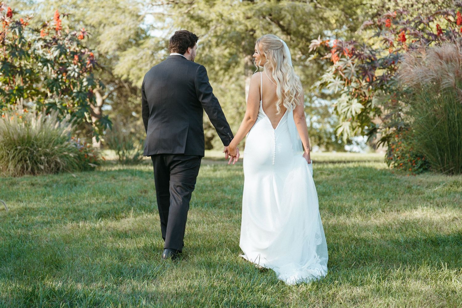 A couple in wedding attire walking through a garden with red berries.