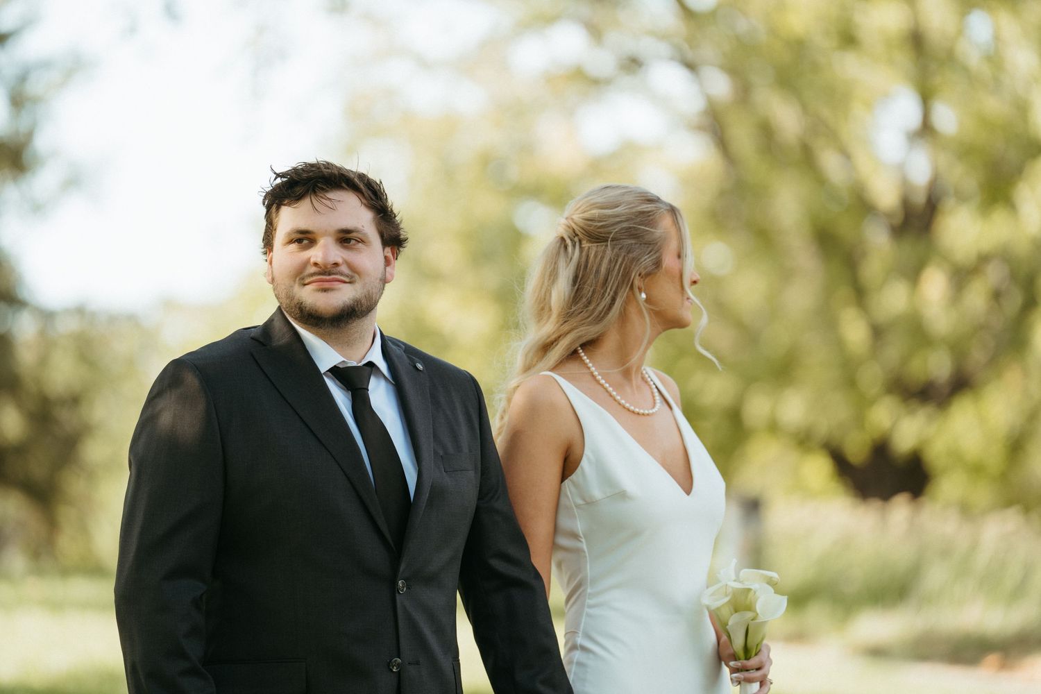 A couple in wedding attire laughing together outdoors on a sunny day.