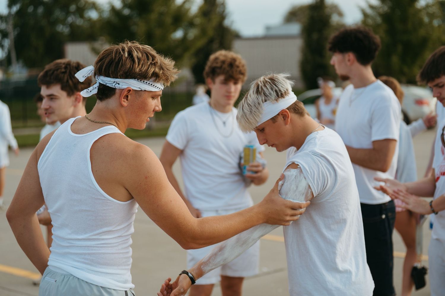 Young men in white outfits with headbands gather outdoors during a casual athletic event on a sunny day.