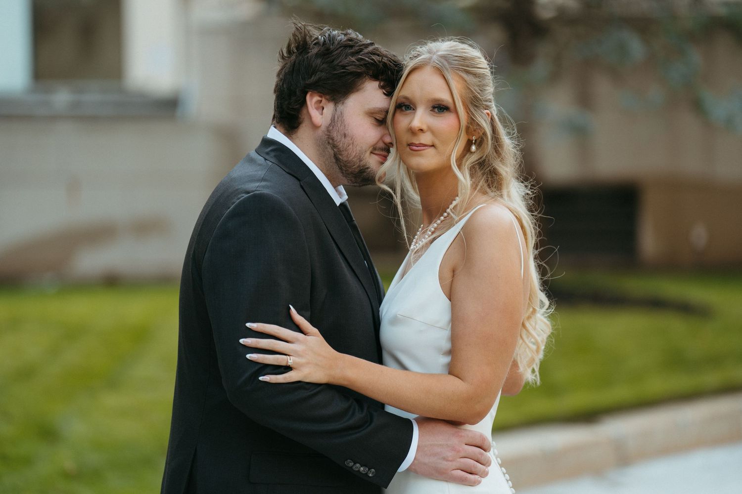 A couple in wedding attire embracing outdoors during a photoshoot.