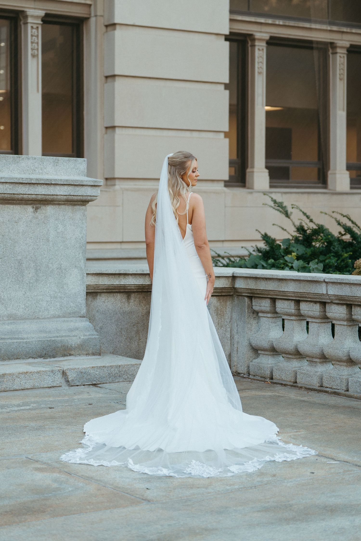 A flowing white wedding dress train spreads elegantly across stone steps.