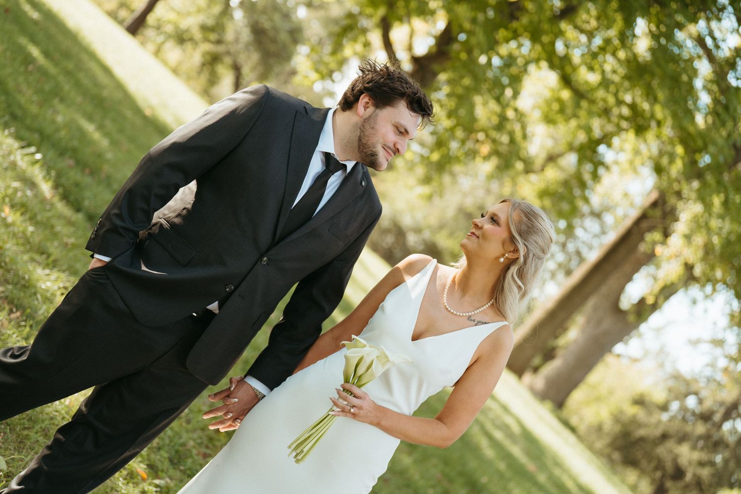 A couple in formal attire sharing a romantic moment under green trees.