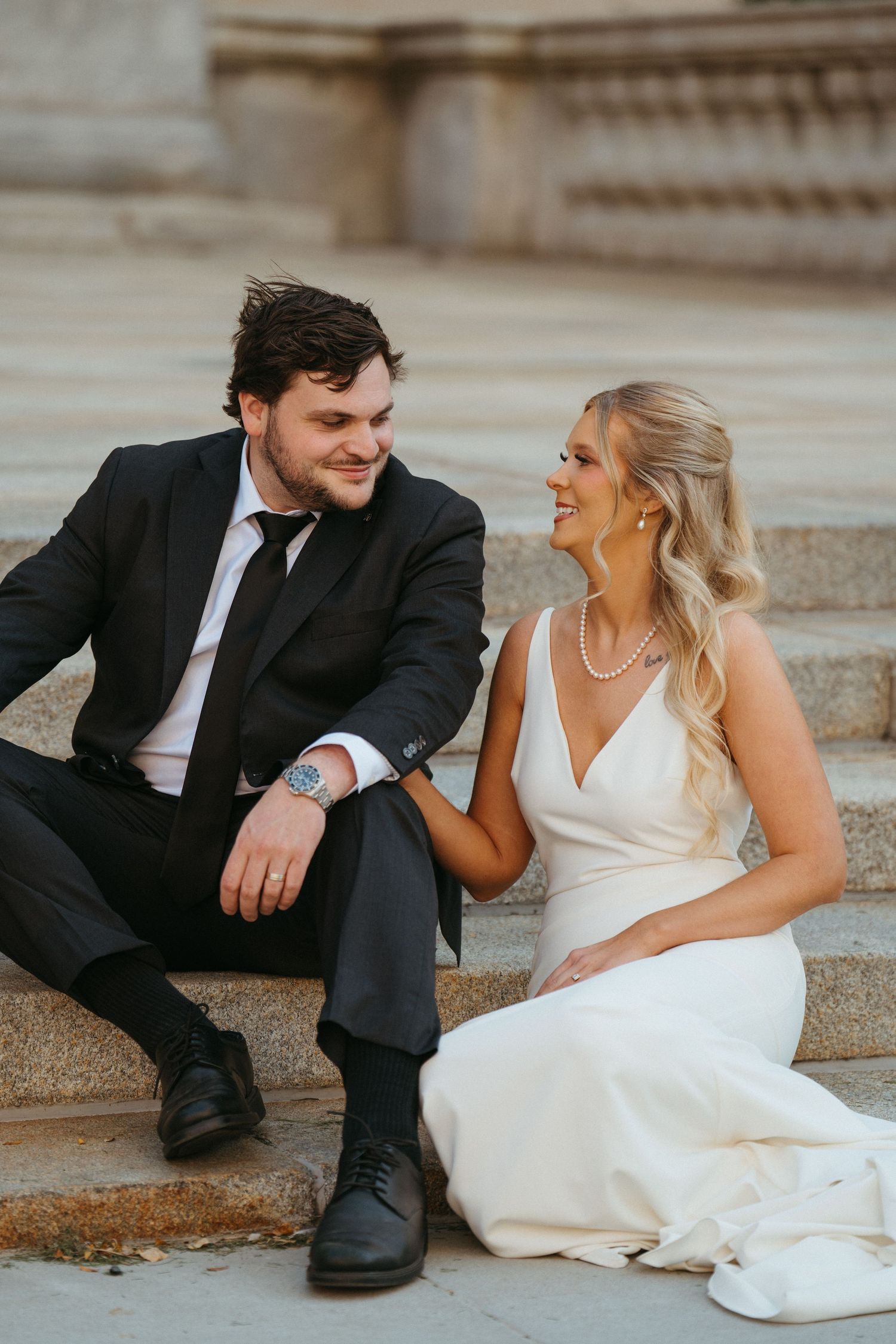 A couple in wedding attire sitting on stone steps sharing candid laughter.