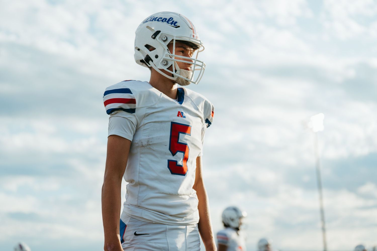Young football player wearing number 5 jersey and white helmet stands on field during game day.