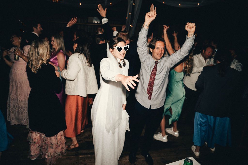 People dancing and celebrating at a lively party with someone wearing sunglasses and a white outfit in the foreground.