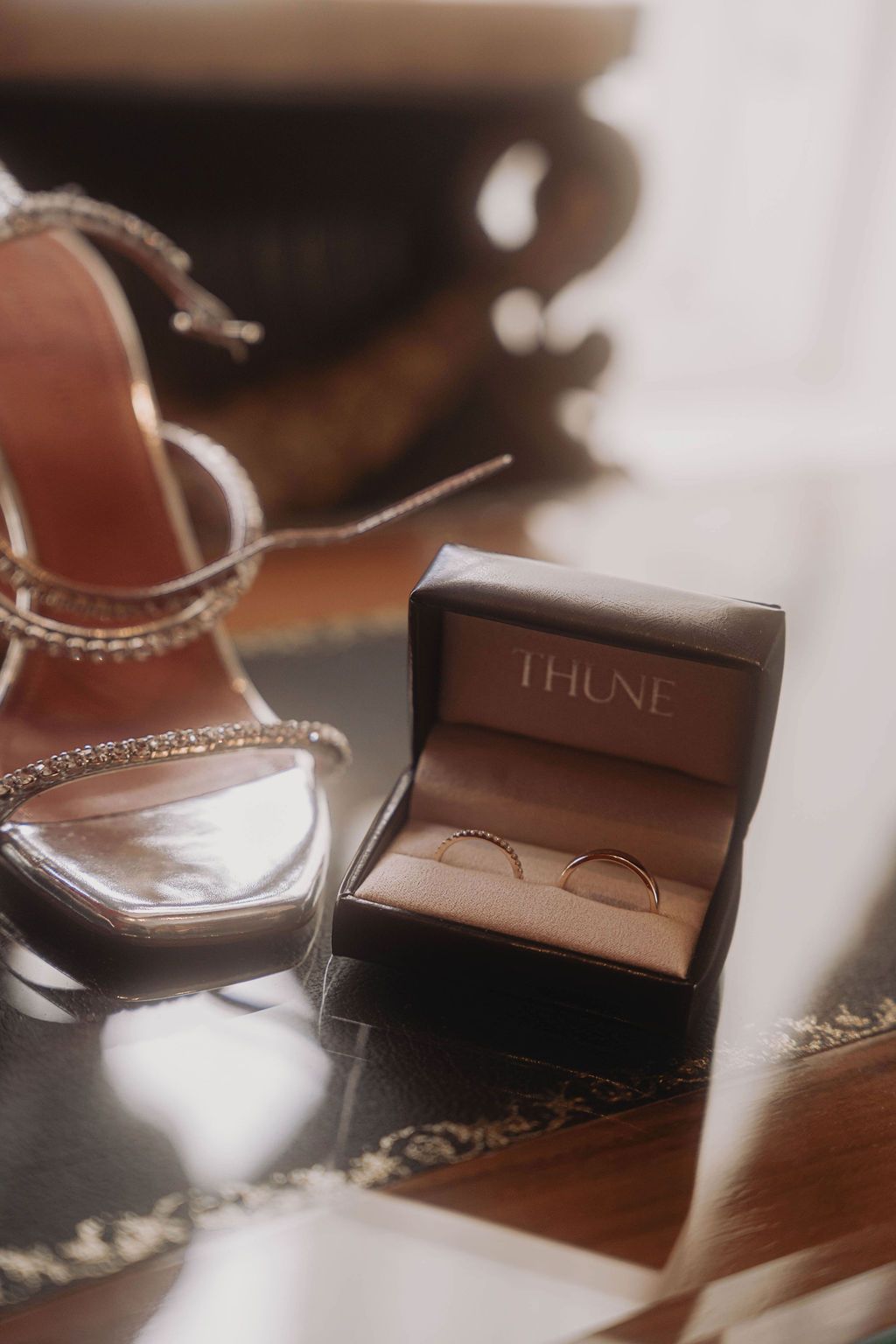 Close-up shot of brown leather wallet and jewelry items arranged on wooden surface in warm lighting.
