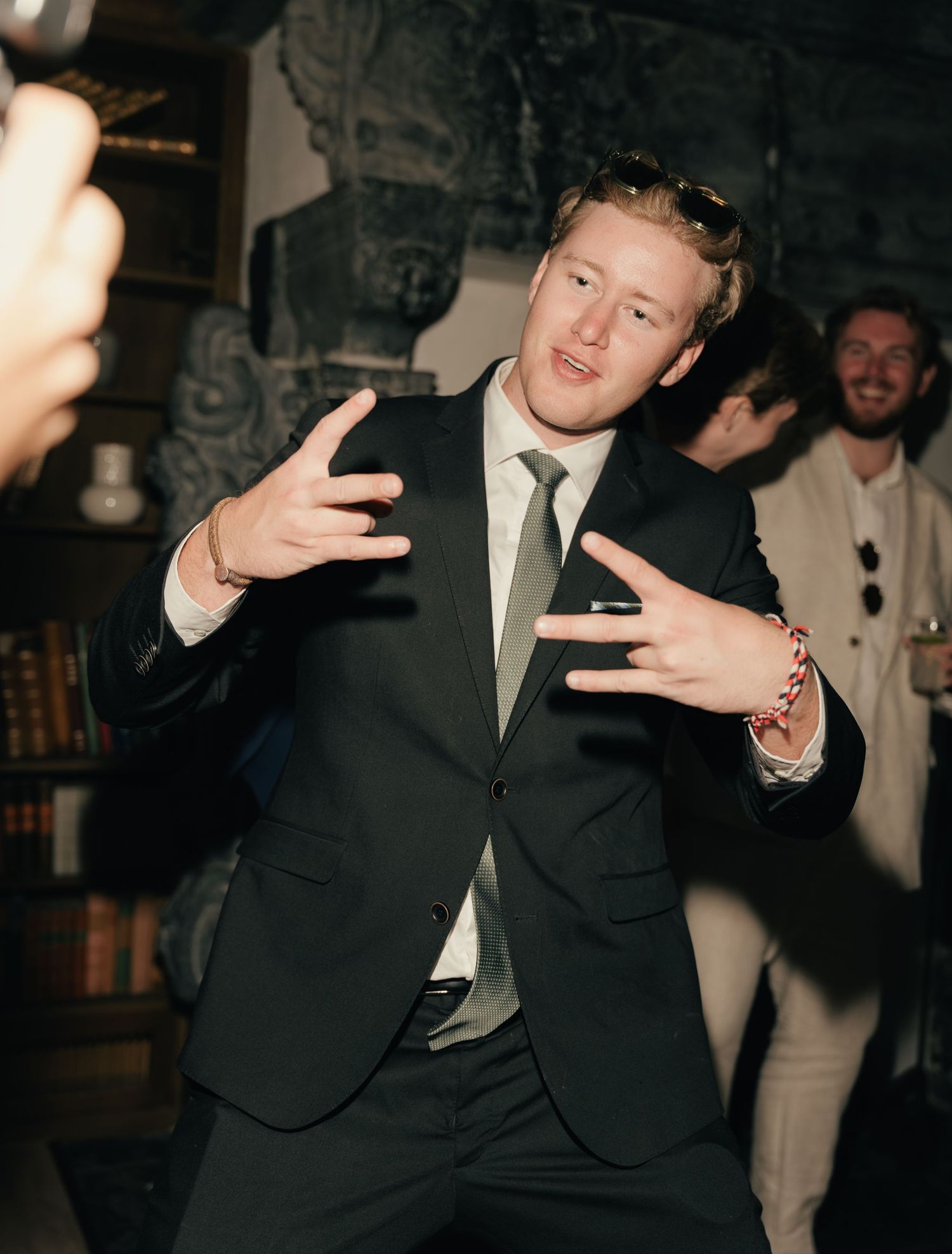 Wedding guest in black suit dancing energetically at indoor wedding reception celebration.
