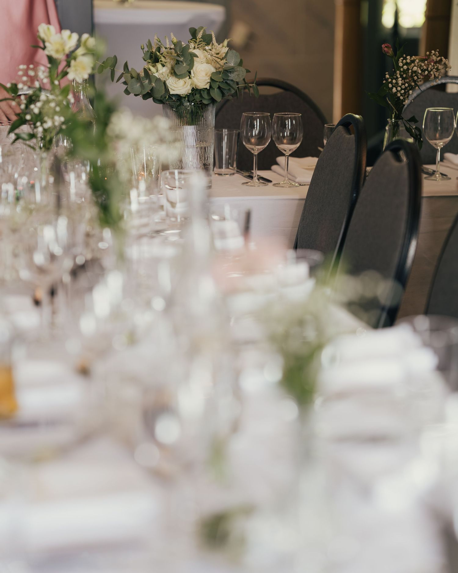 Elegant wedding reception table set with white linens, glassware, and white floral centerpieces.