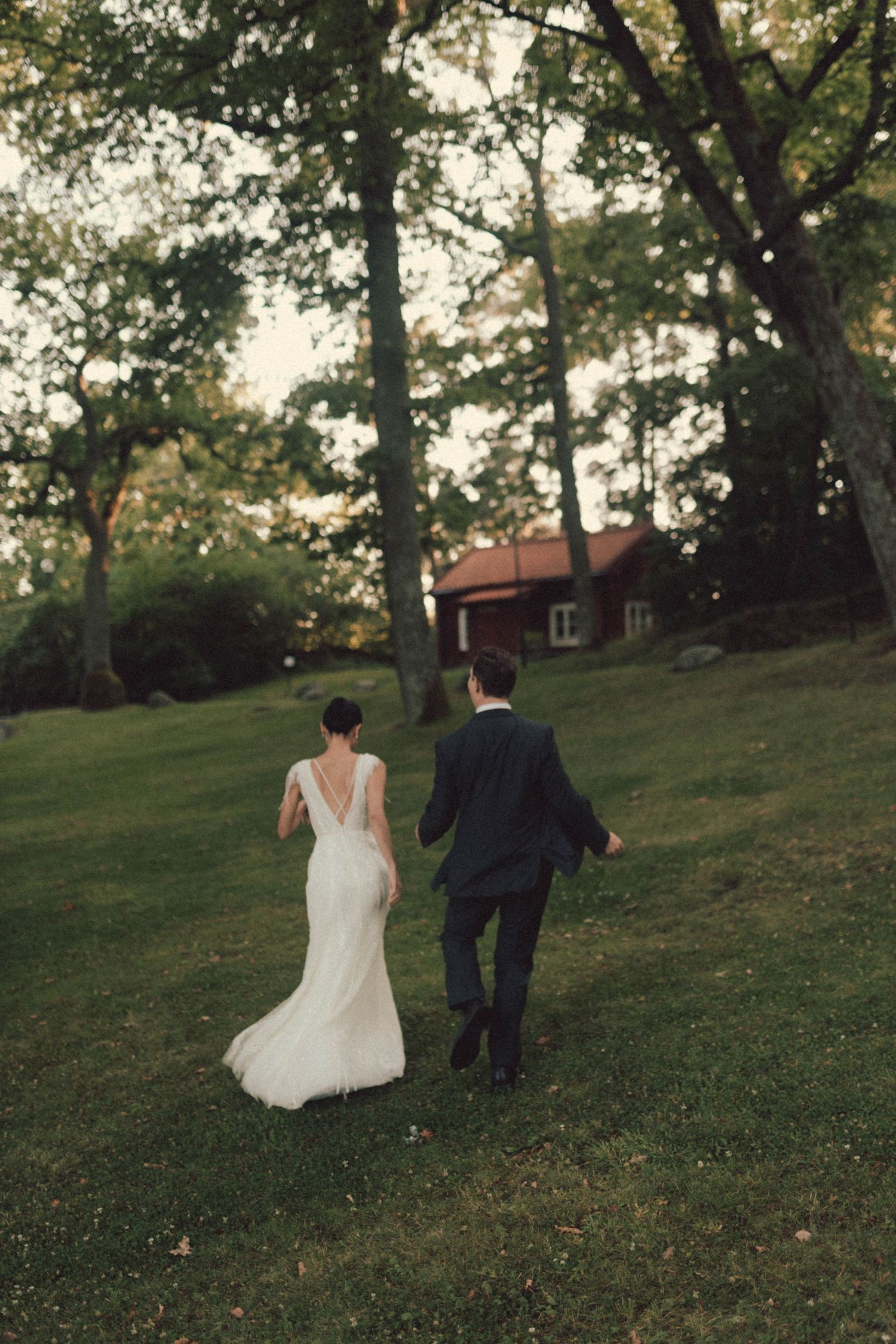 Newlywed couple walks hand in hand up a grassy hill surrounded by trees at sunset during their outdoor wedding.